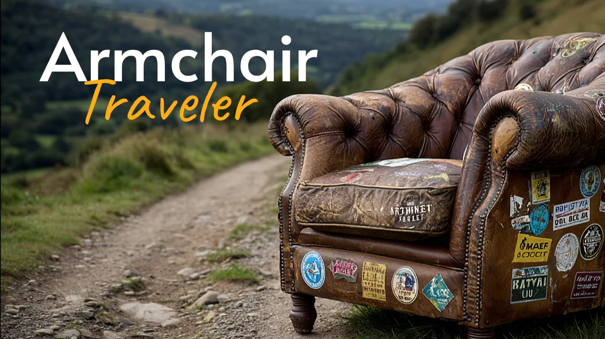 An image of a weathered leather armchair with tufted buttons is covered in world travel stickers and sitting on the side of a two-track road on a nature covered hill-top. Titled Armchair Traveler.