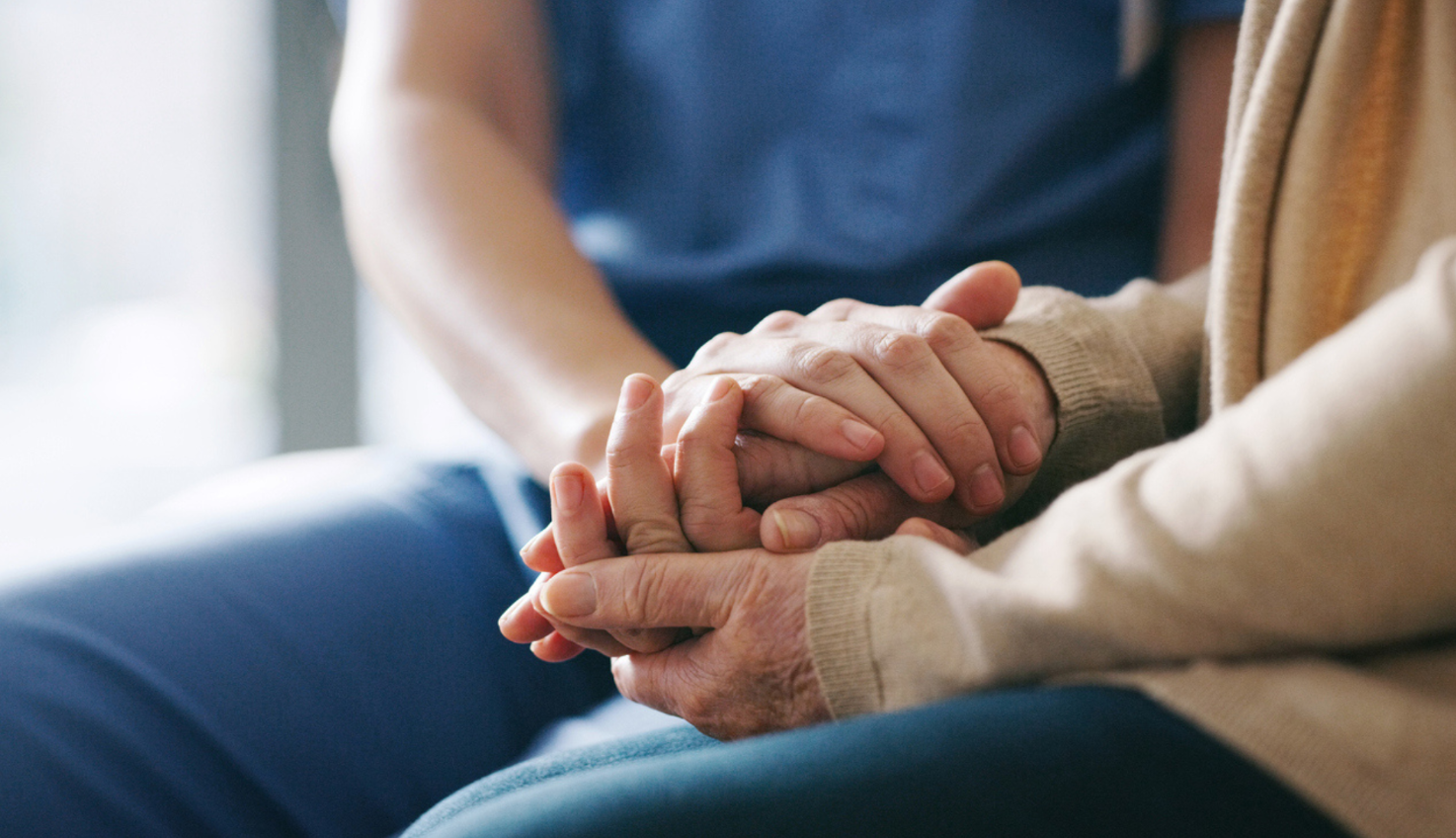 A photo of spouse of an elder patient locking hands with a registered nurse in a caring way.