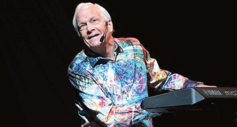 A photograph of musical artist and pianist, Ken Medema, sitting and playing at a keyboard while singing to an audience.