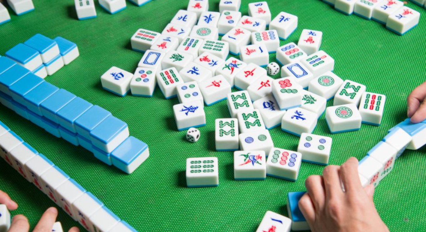 A felted table with 4 sets of Mahjong tiles in front of four players.