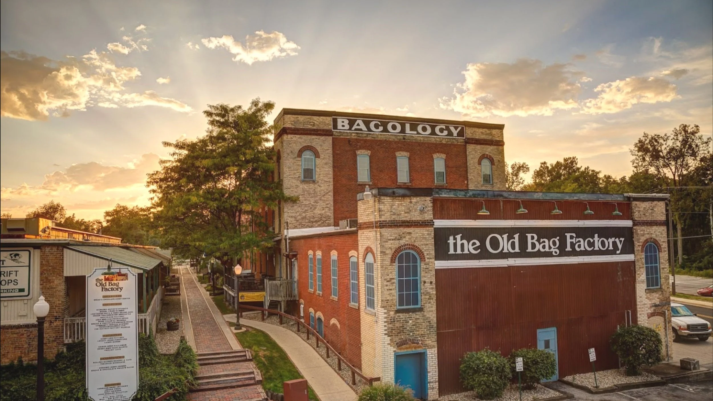 A photograph displaying the historic Old Bag Factory building in the heart of Goshen, Indiana set to a clear sky with only a few clouds and warm sunlight peaking from behind the building.