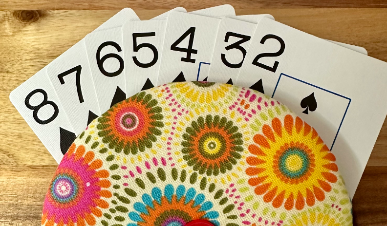A photo of a hand of playing cards sandwiched between two discs wrapped in fabric and held together with a button. Designed to view and hold your card hand comfortably.