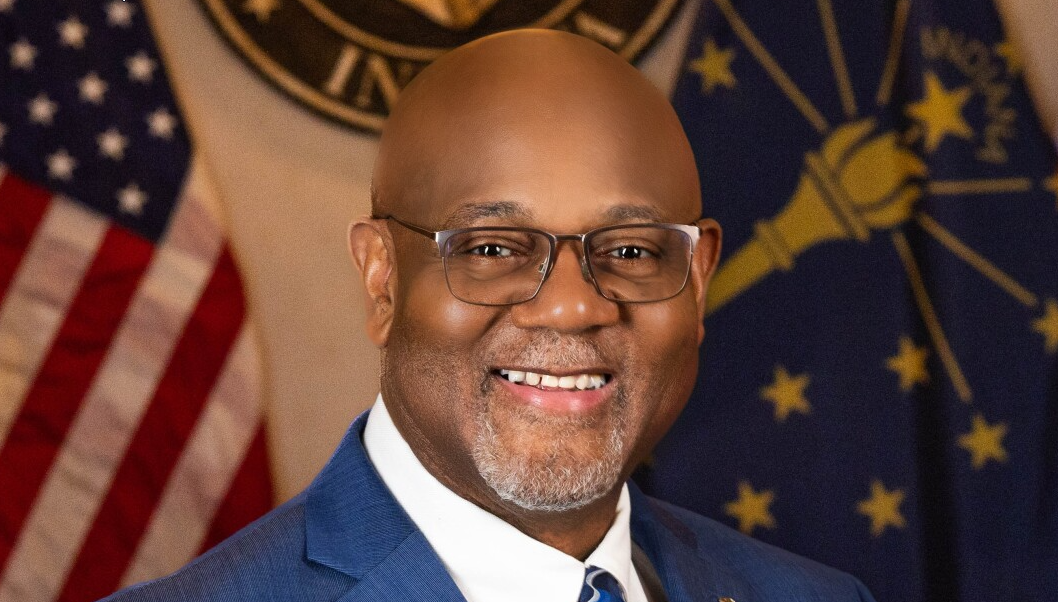 Photo of Mayor, Rod Roberson posing for a photo in a suit and tie in front of the Elkhart City Seal, City flag, and American flag.