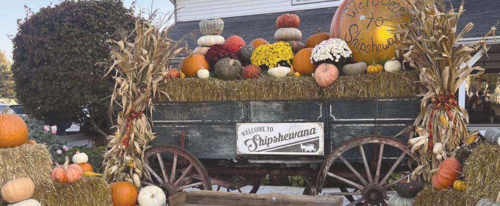 A time-period horse wagon full of straw and pumpkins in a cozy fall setting with the sign attached titled "Welcome to Shipshewana" in the small town of Indiana.
